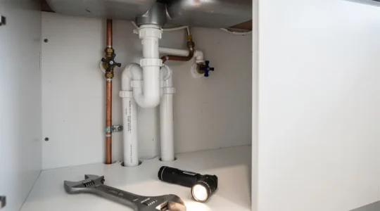 Plombier examinant des canalisations sous un évier avec outils professionnels